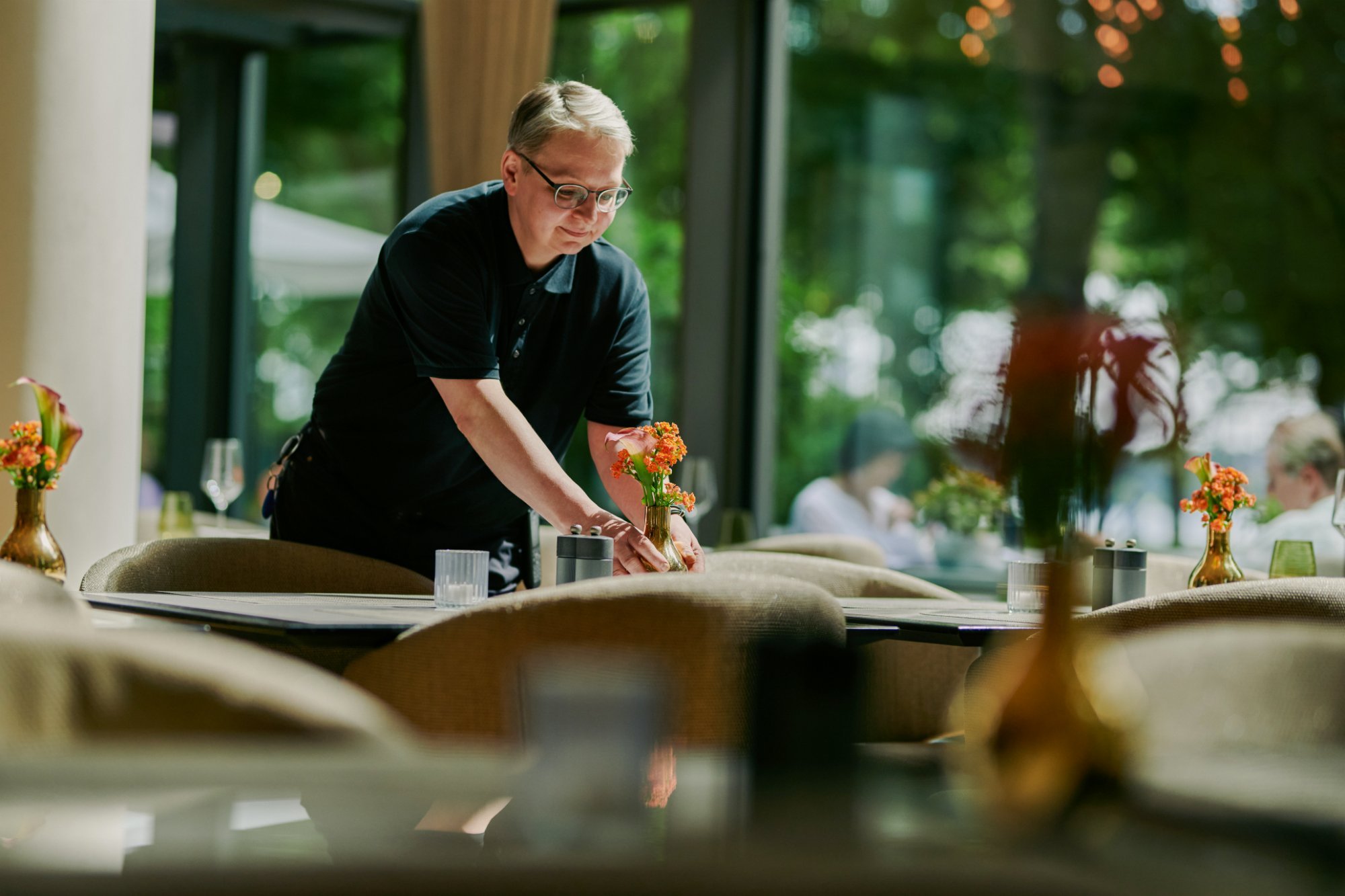 Waiter arranging table flowers, restaurant terrace